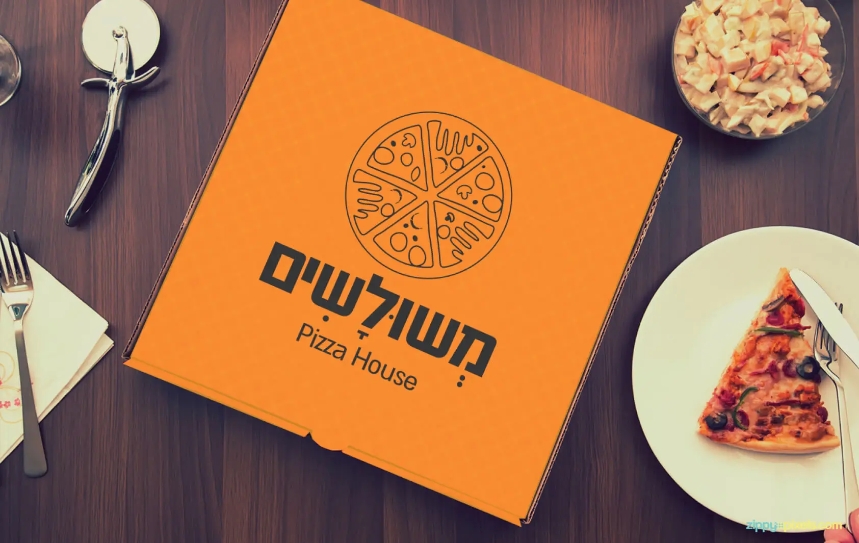 מוקאפ קופסת פיצה כתומה עם לוגו משולשים על שולחן עץ לצד פרוסת פיצה וקערה של סלט