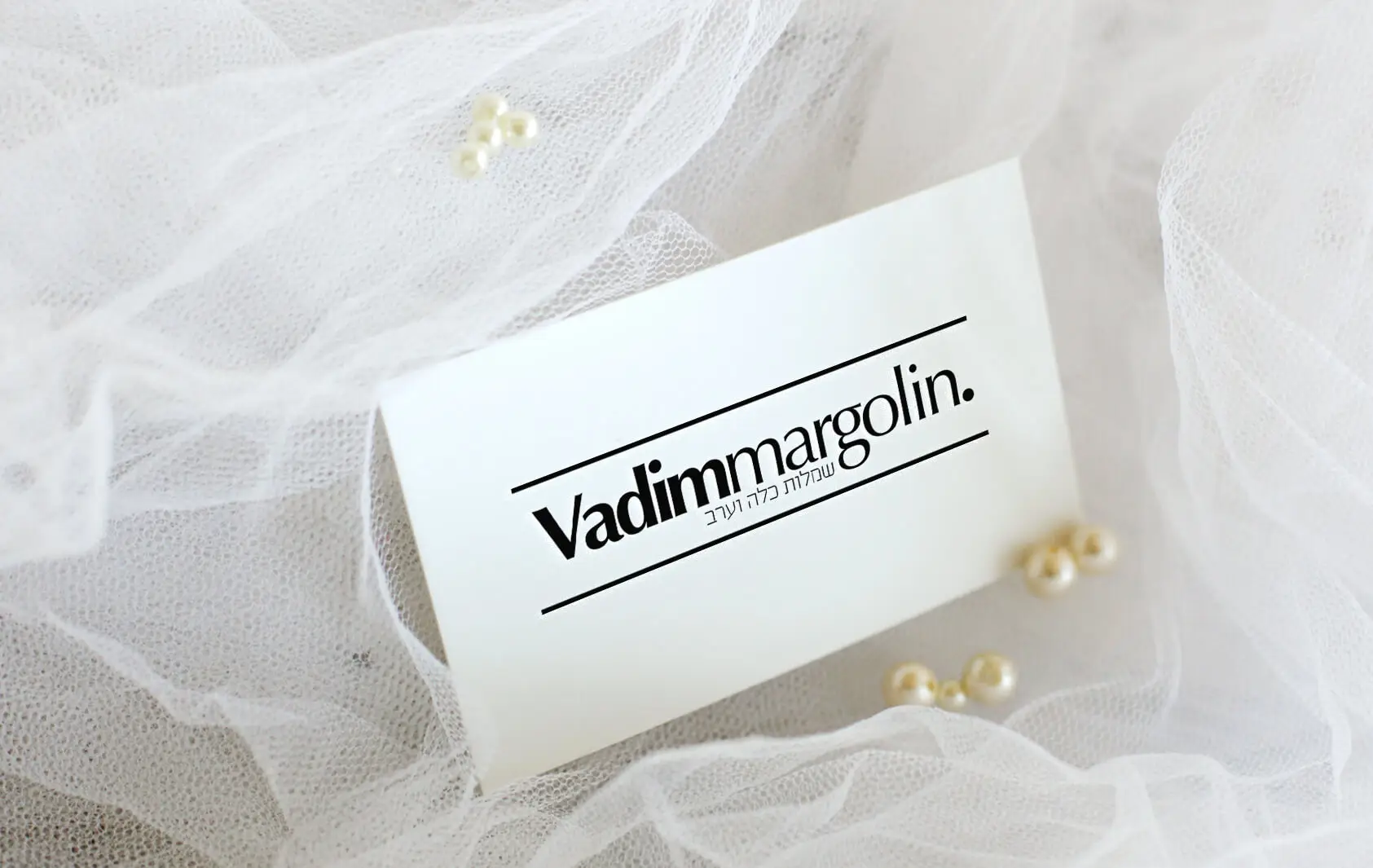 מוקאפ כרטיס ביקור מגולגל עם לוגו Vadim Margolin על רקע תחרה לבנה ופנינים