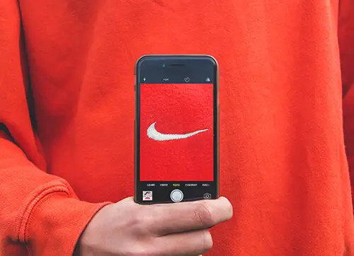 אדם בסוודר כתום מחזיק טלפון חכם עם תמונת לוגו Nike על מסך